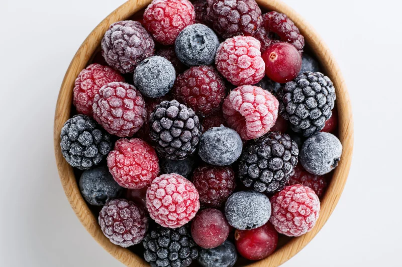 Mixed frozen berries in a wooden bowl viewed from above on white background