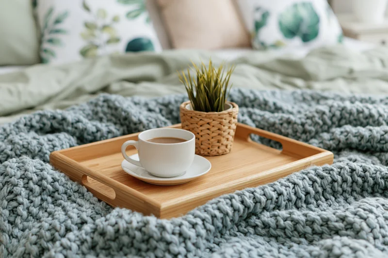 Wooden tray with coffee cup and small plant on a knitted blanket on a bed
