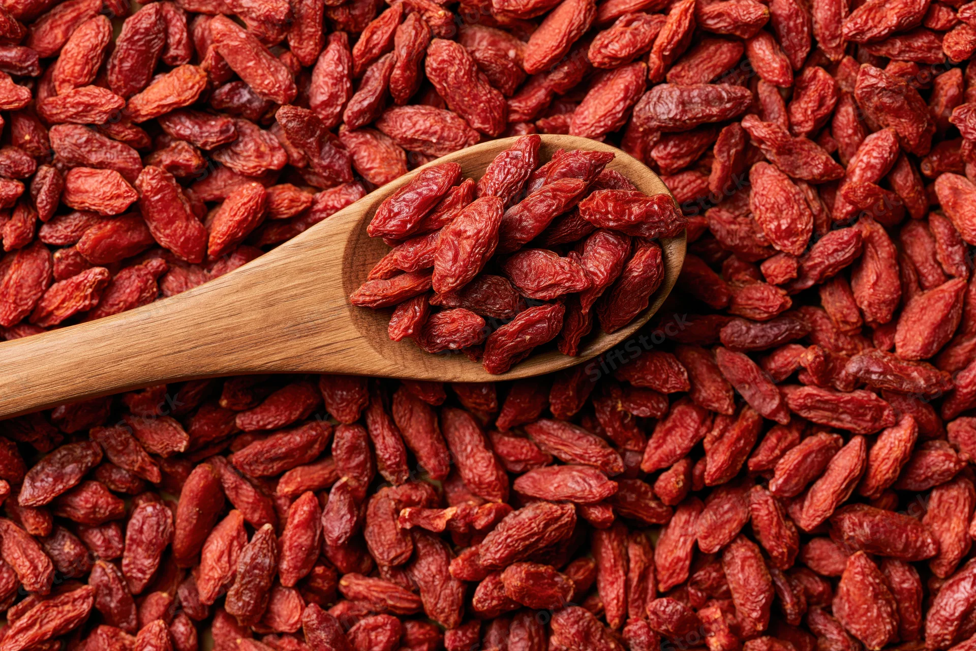 Wooden spoon holding dried goji berries on a flat lay of the same berries