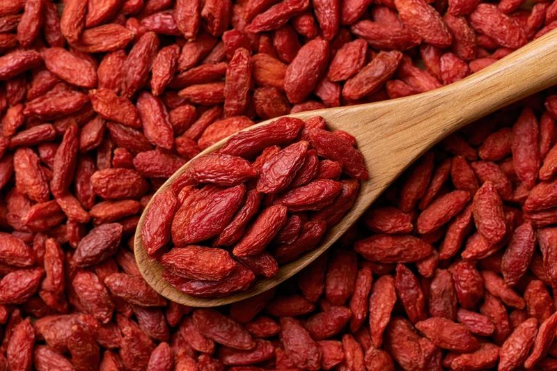 Wooden spoon holding dried goji berries on a bed of the same berries in a flat lay arrangement