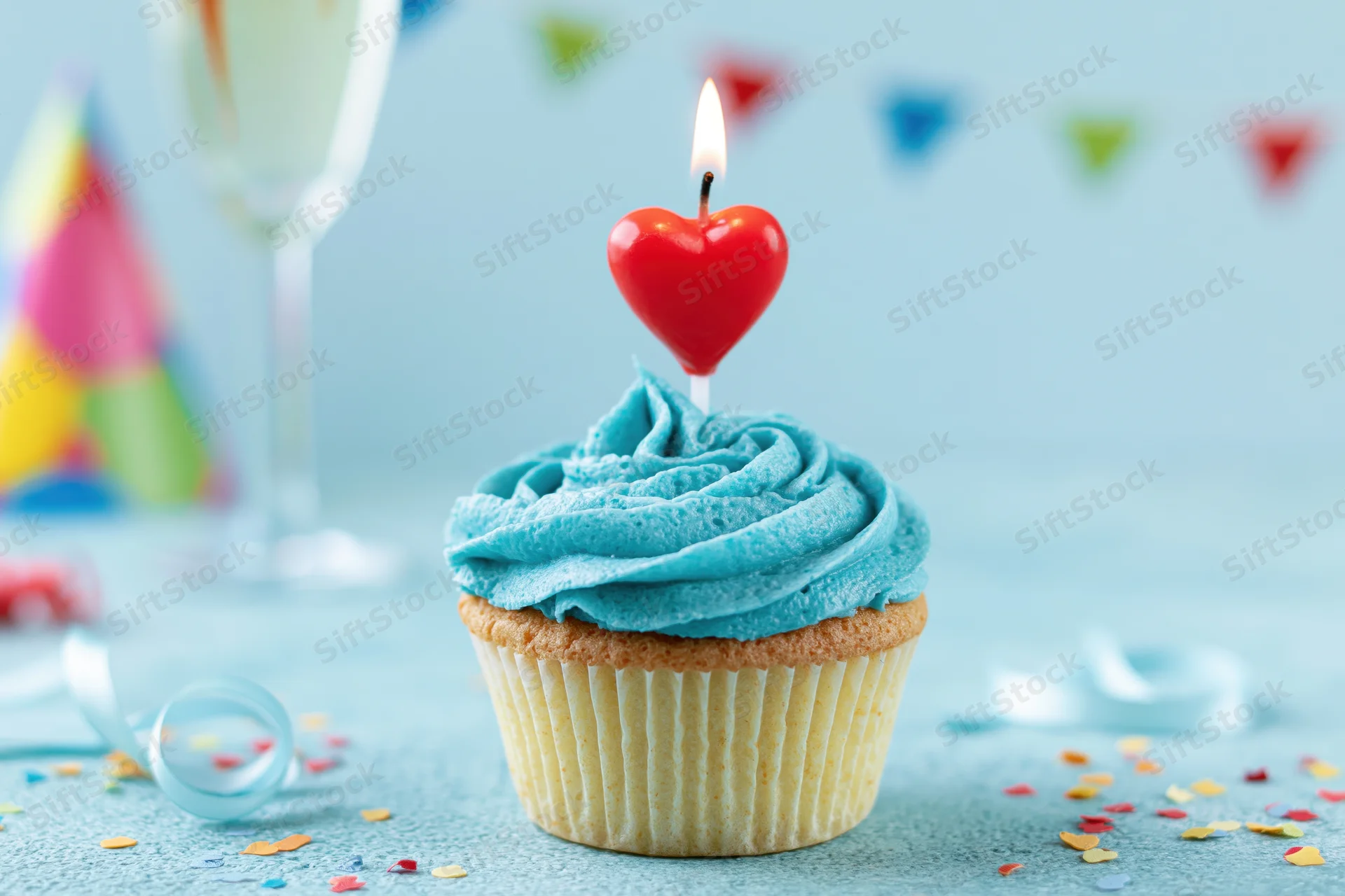 Birthday cupcake with blue frosting and red heart candle on a table with party decorations