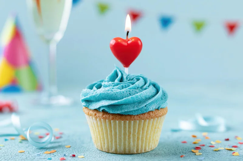 Birthday cupcake with blue frosting and red heart candle on a table with party decorations