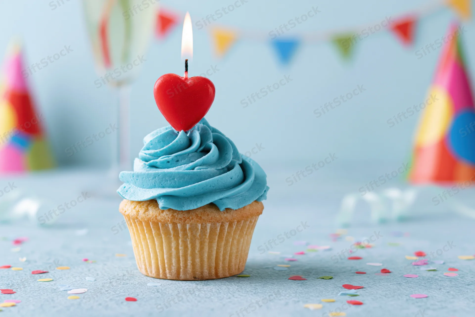 Birthday cupcake with blue frosting and lit red heart candle on a decorated table