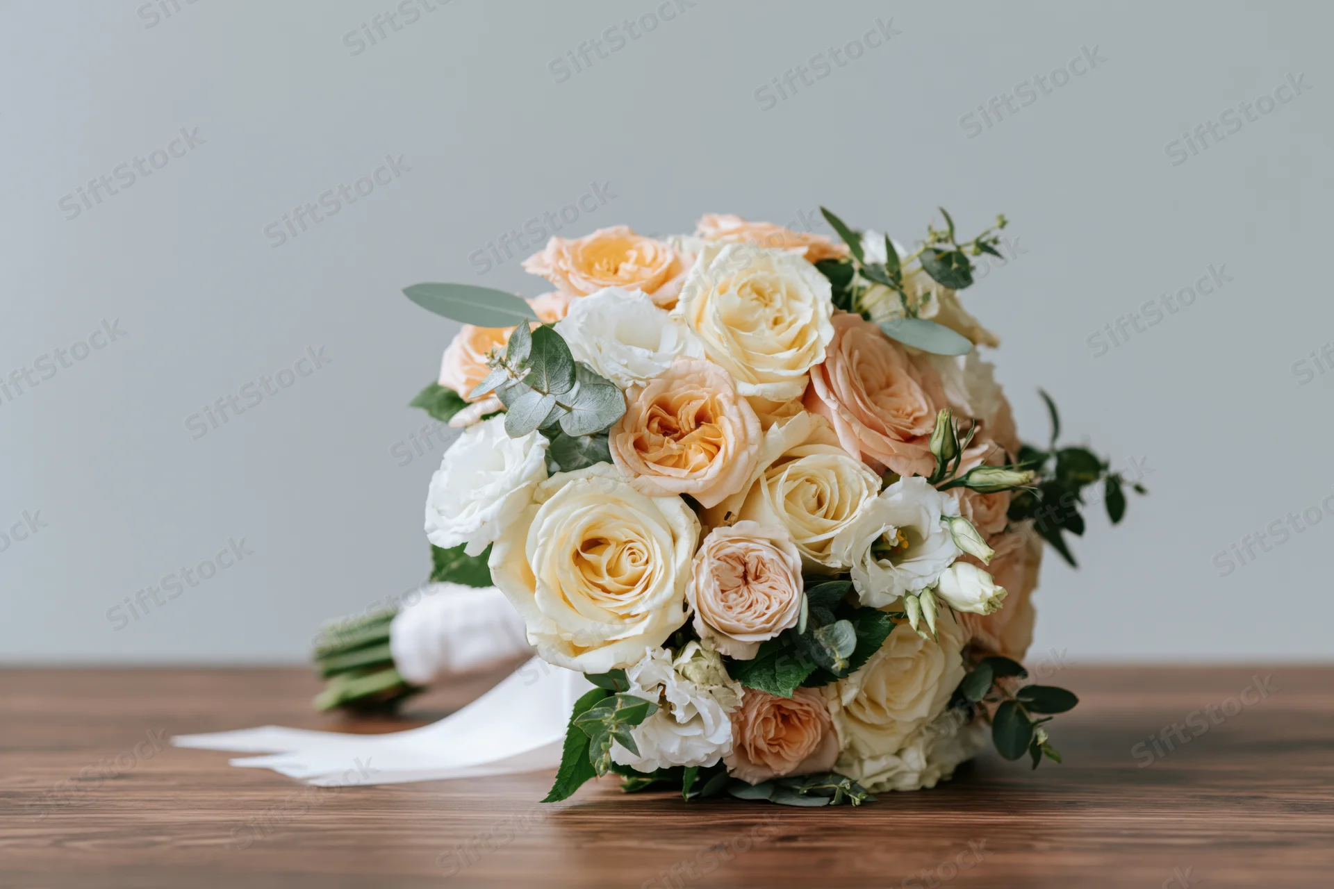 Bridal bouquet of peach and cream roses with greenery resting on wooden surface