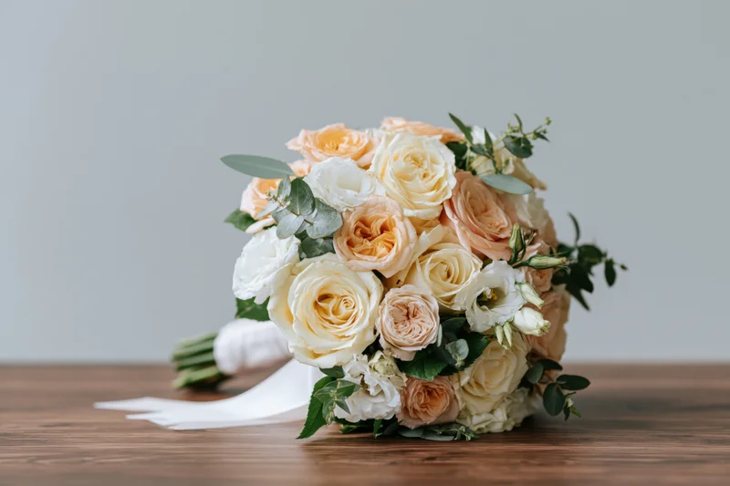Bridal bouquet of peach and cream roses with greenery resting on wooden surface