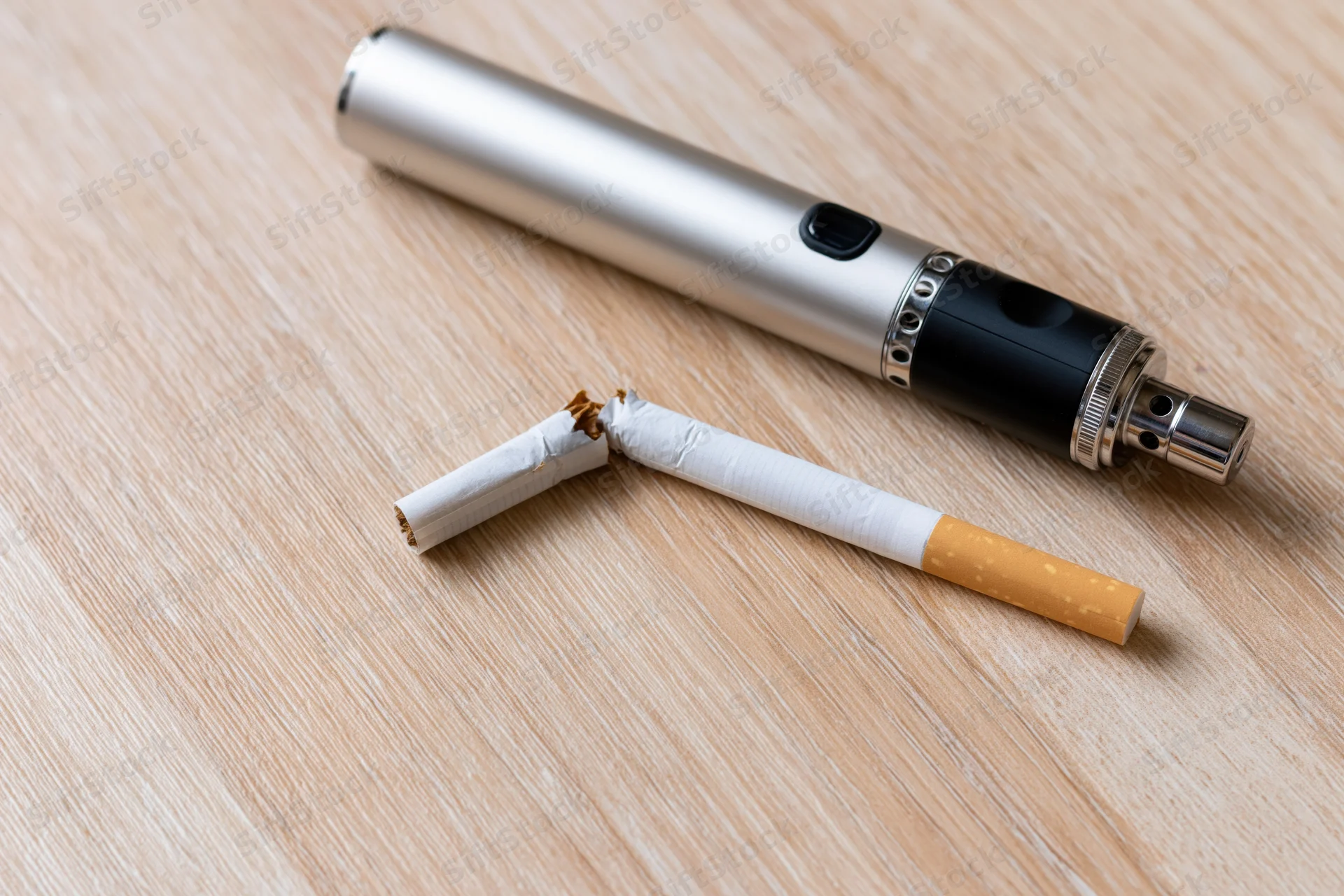 Broken cigarette next to a silver vape device on a wooden table