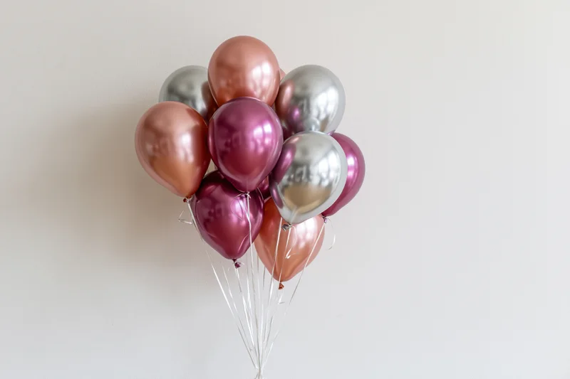 Metallic helium balloons clustered together against a plain wall
