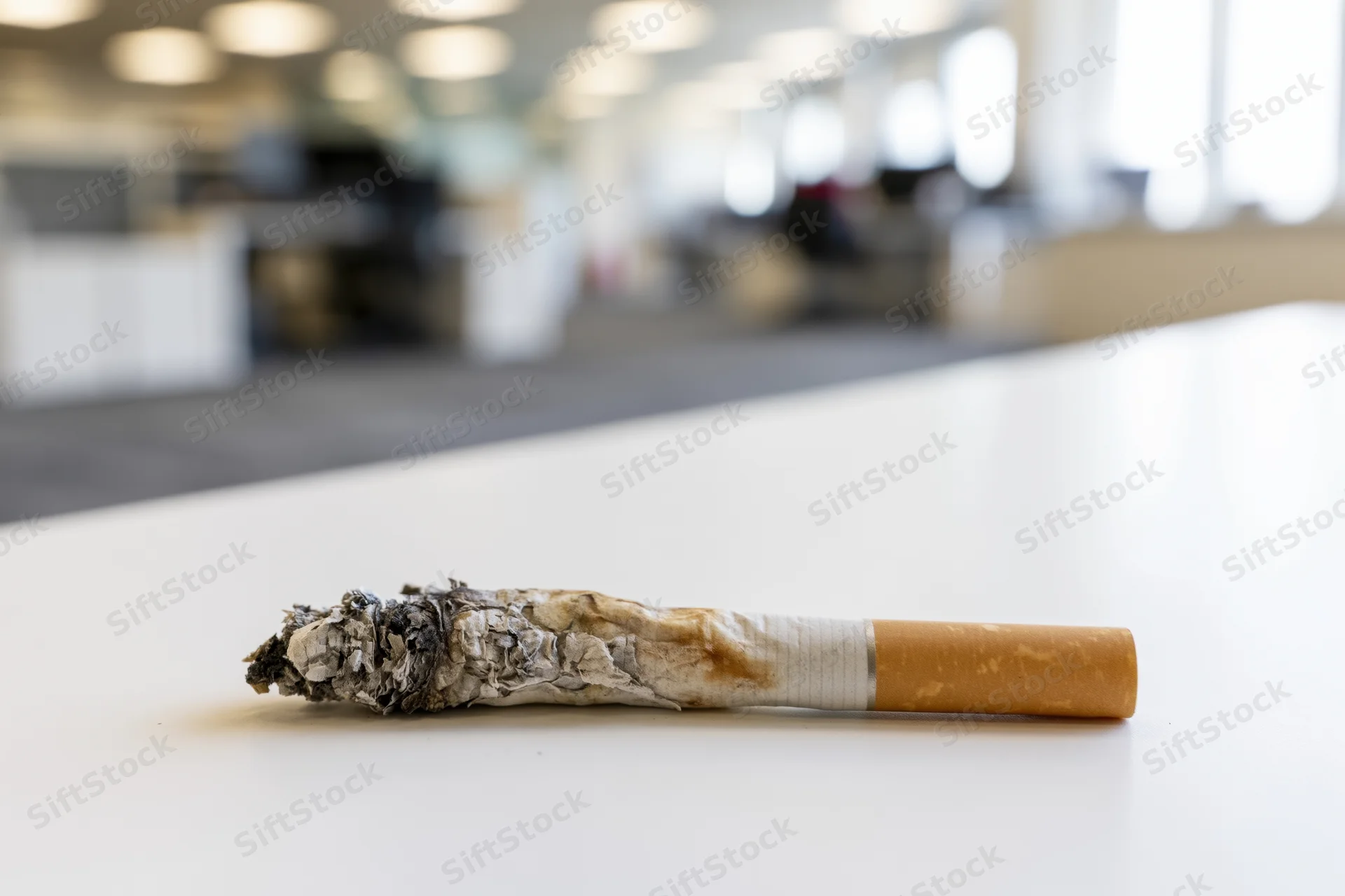Burnt cigarette with ash resting on white office desk