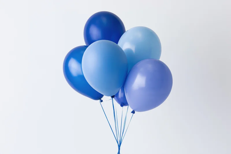Cluster of blue helium balloons floating against white background with copyspace