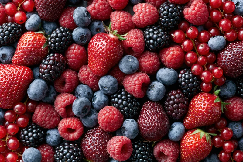 A dense flat-lay of mixed fresh berries including strawberries, raspberries, blueberries, blackberries and redcurrants covering the frame