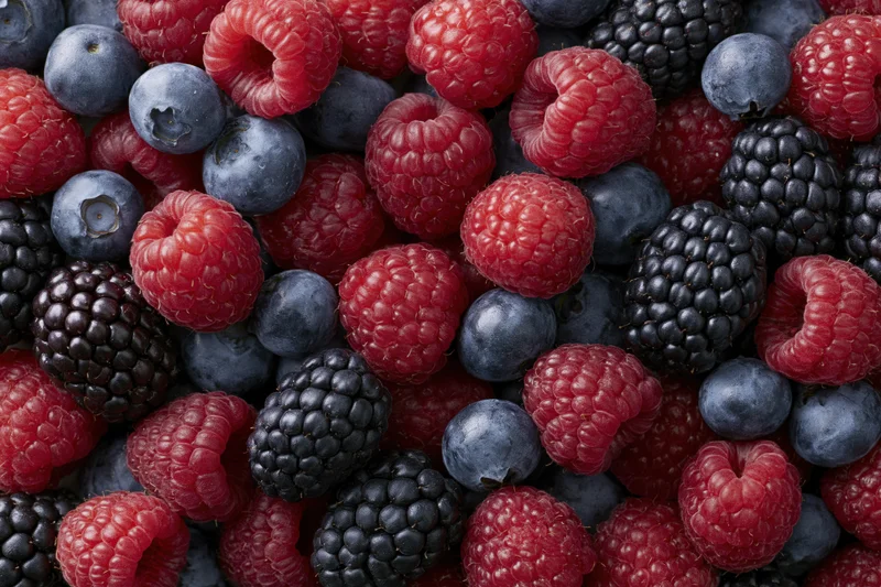 Closeup of fresh mixed berries including raspberries blueberries and blackberries arranged in a dense flat lay