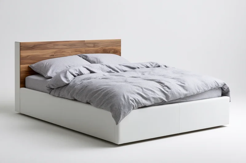 Double bed with white faux-leather frame and wooden headboard, unmade with gray bedding, isolated on white background