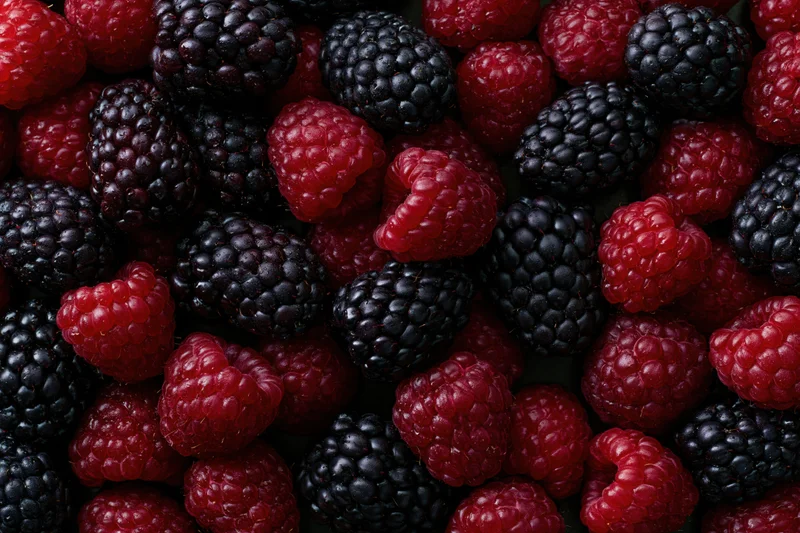 Closeup of fresh raspberries and blackberries scattered in a flat lay arrangement