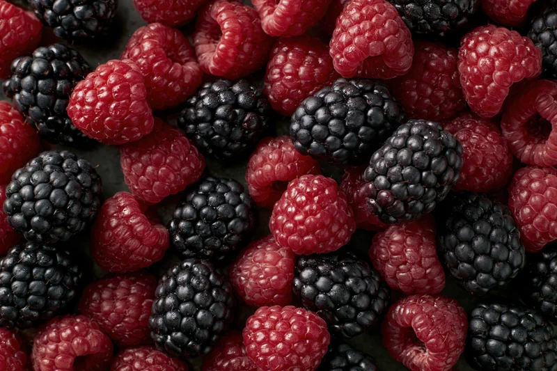 Fresh raspberries and blackberries scattered in a flat lay on a dark surface