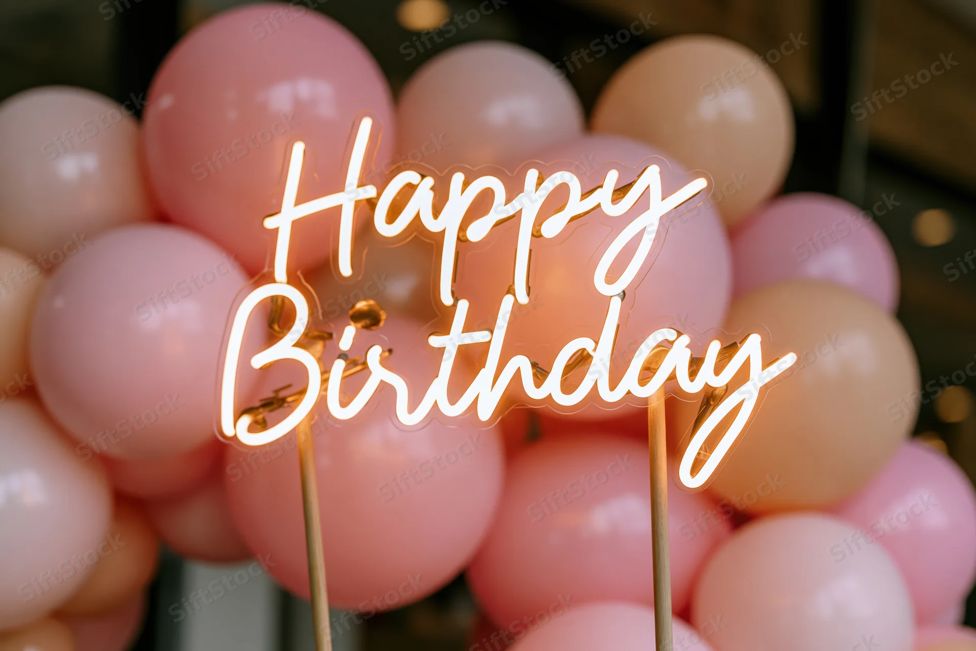 Glowing neon happy birthday sign on wooden sticks in front of pink balloons
