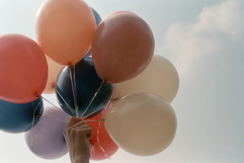 Hand holding a cluster of pastel-colored helium balloons against a cloudy sky