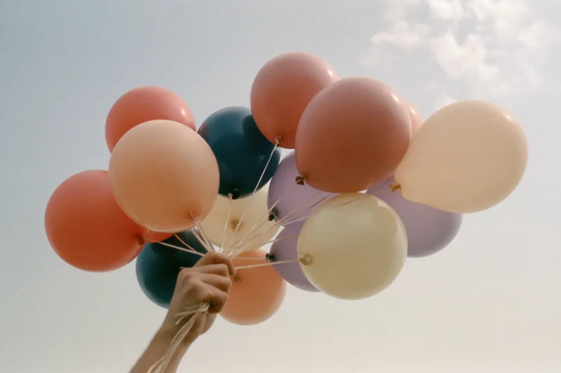 Hand holding a cluster of pastel helium balloons against a cloudy sky