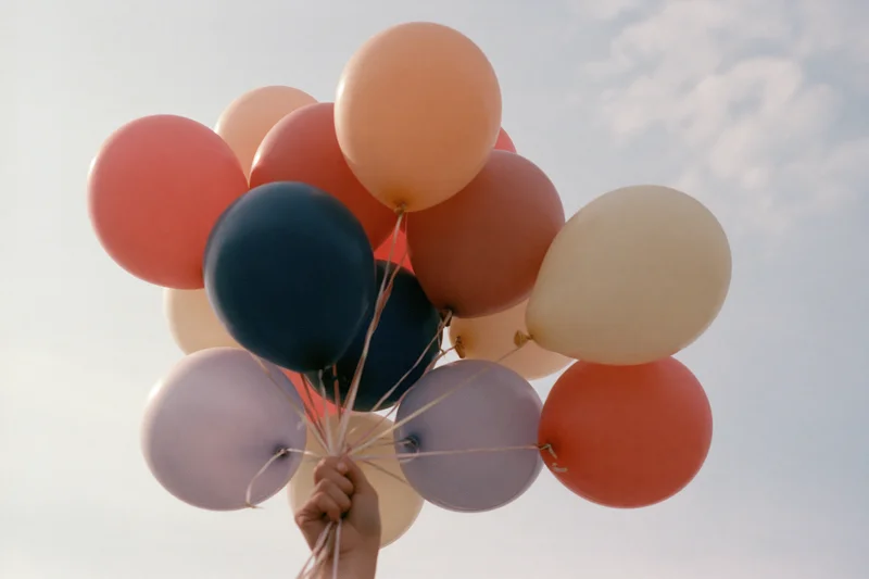Hand gripping a cluster of helium balloons against a cloudy sky