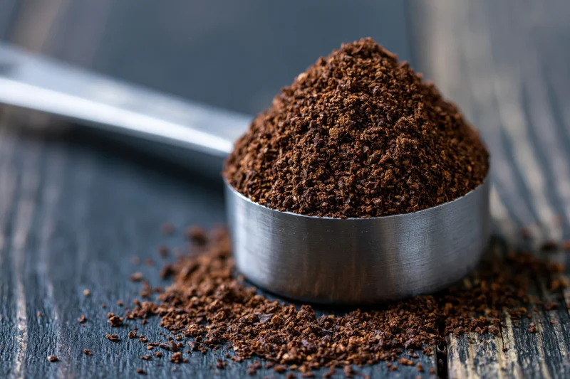 Heaping metal measuring spoon filled with coarse ground coffee on dark wooden surface