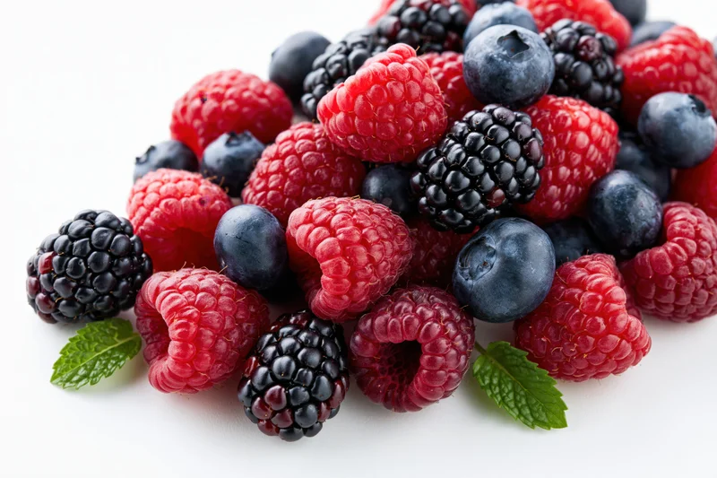 A pile of fresh raspberries, blackberries and blueberries with mint leaves on white background
