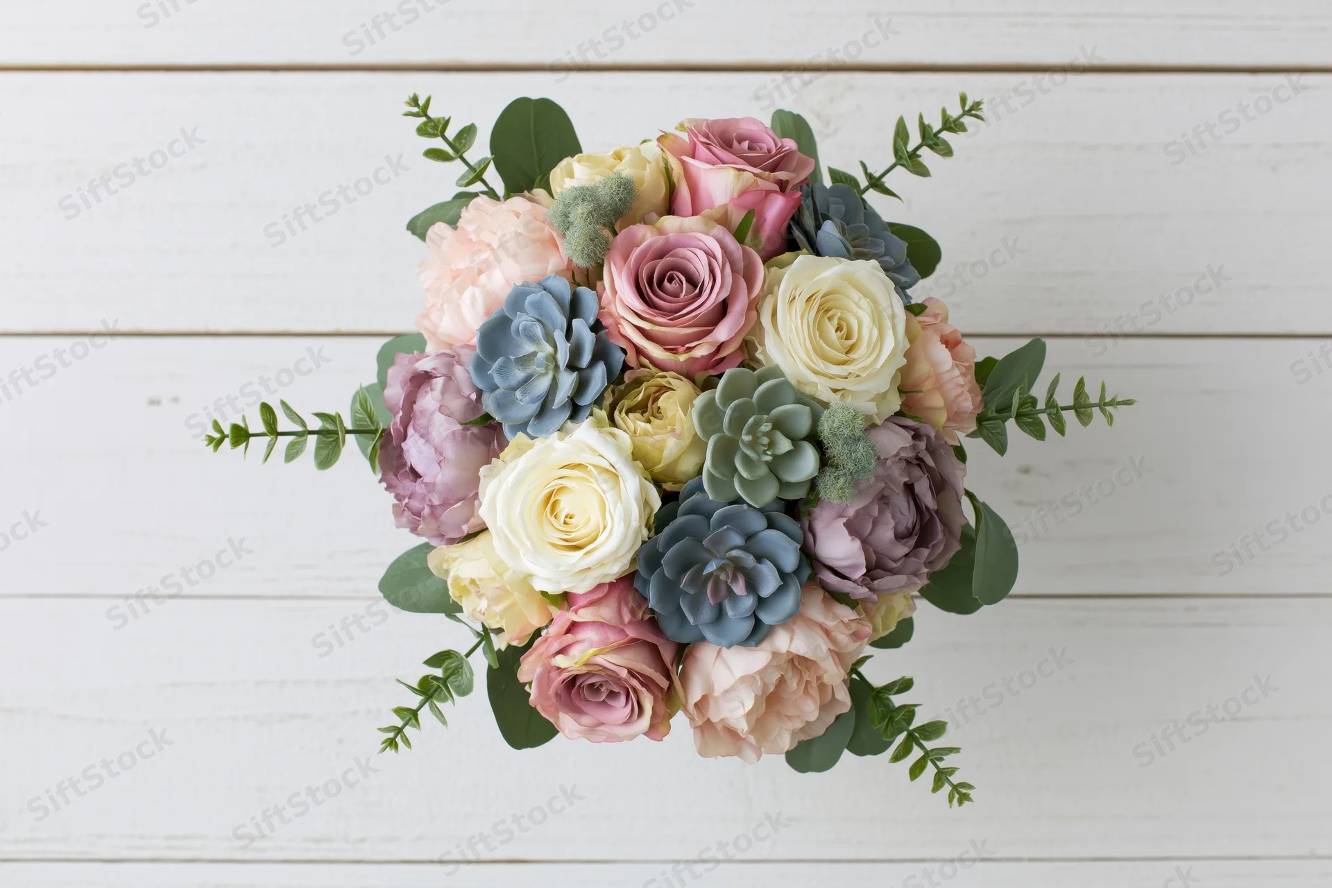 Mixed floral bouquet with roses and succulents arranged in dome shape on white wooden surface