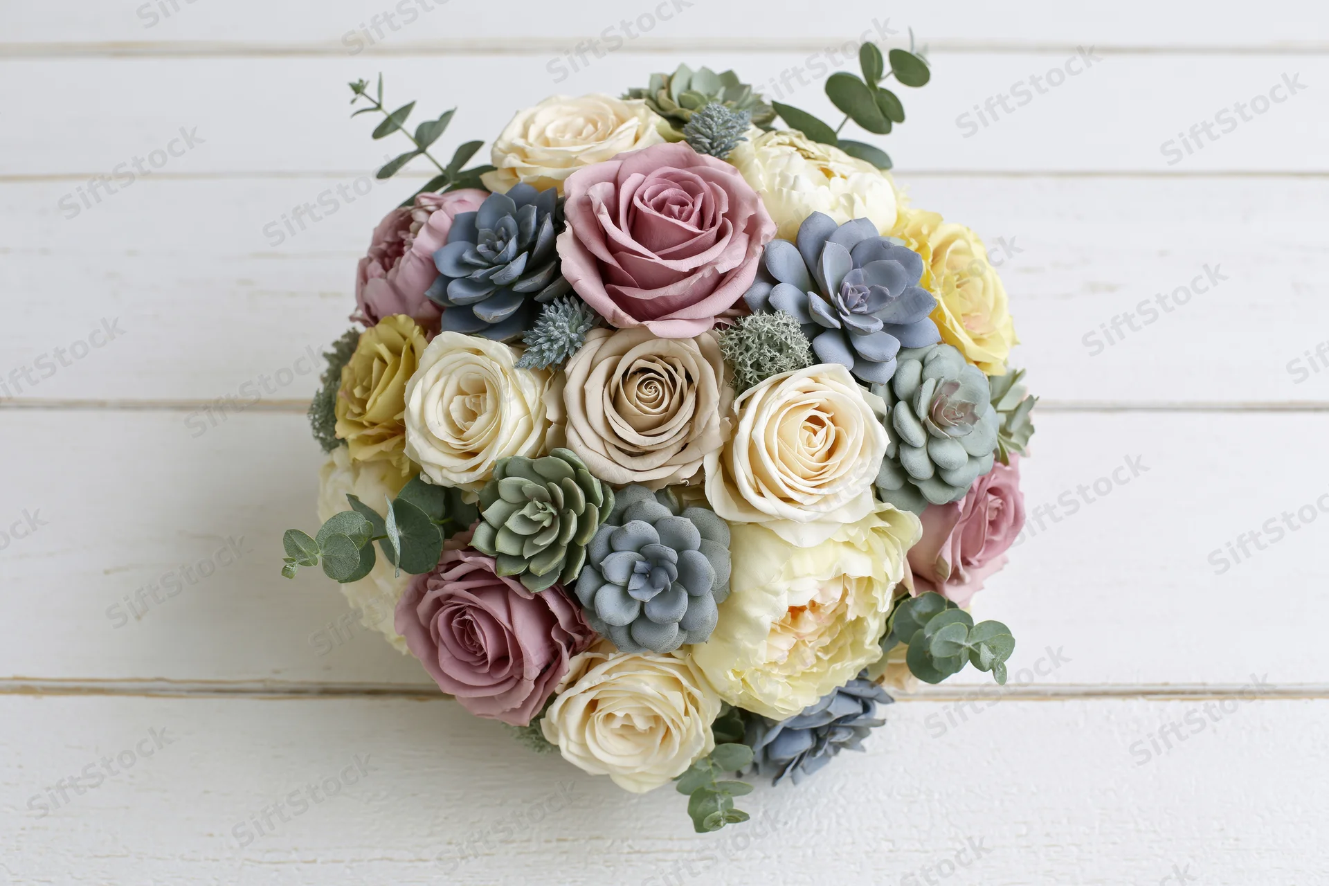 Mixed floral bouquet with roses and succulents arranged in a rounded dome on a white wooden surface