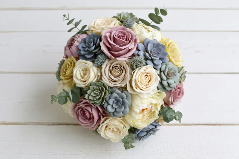 Mixed floral bouquet with roses and succulents arranged in a rounded dome on a white wooden surface
