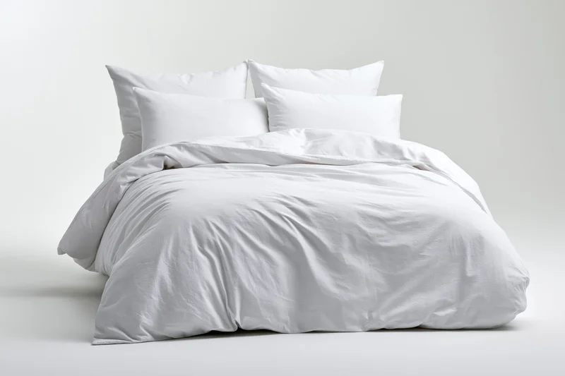 White bed with four pillows and comforter on plain background