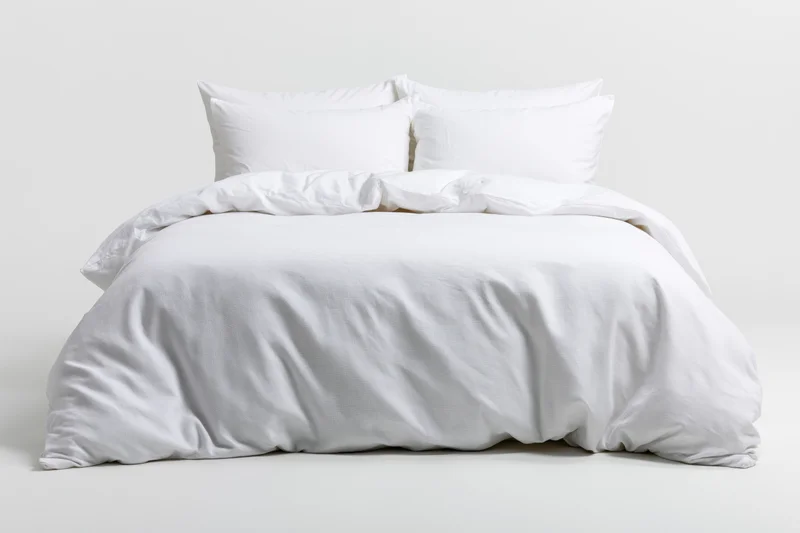White bed with four pillows and duvet on plain background