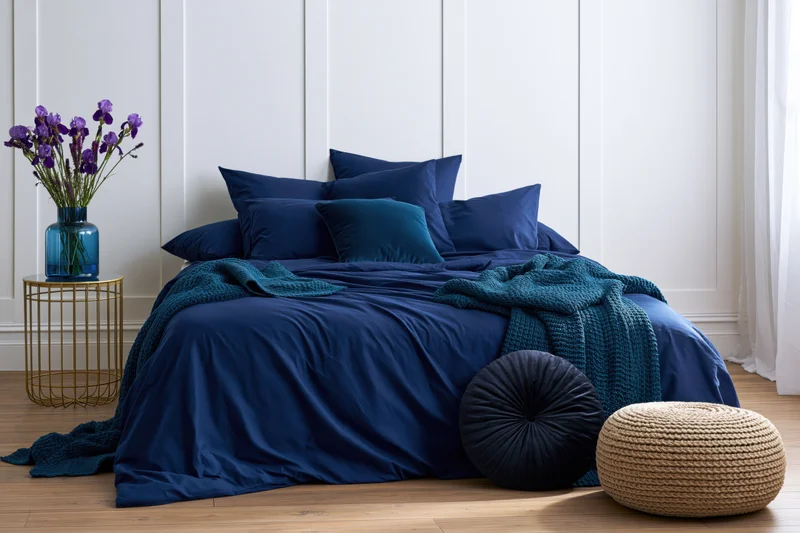 Neatly made double bed with navy blue bedding and decorative pillows in a modern bedroom with white paneling and wooden floor