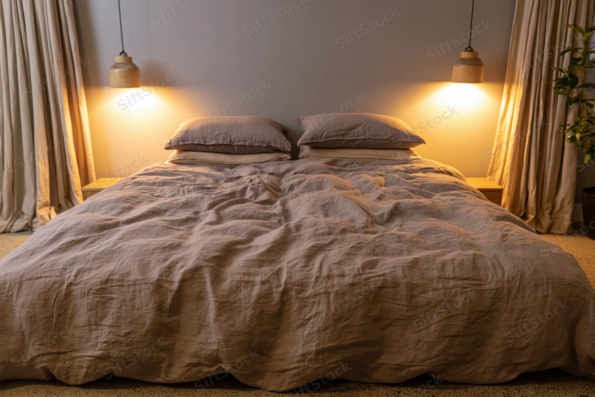 Rumpled linen duvet on a queen bed with pendant lights and curtains in a cozy bedroom