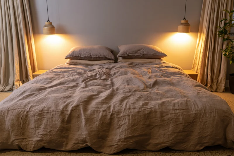Rumpled linen duvet on a queen bed with pendant lights and curtains in a cozy bedroom