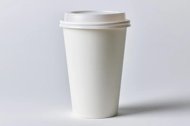 White disposable paper coffee cup with plastic lid on plain background