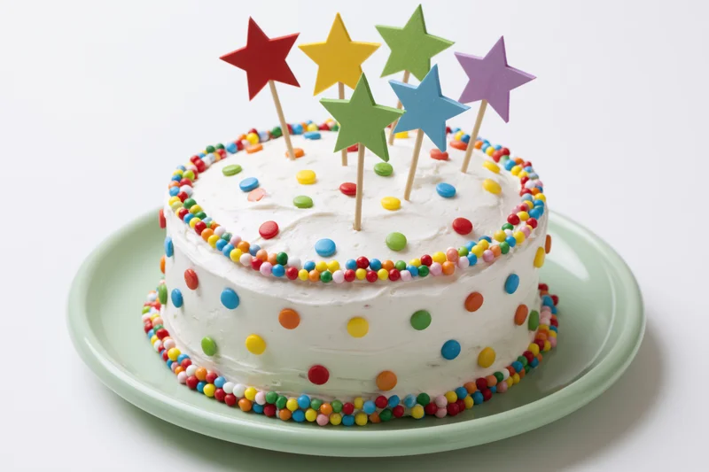 Round white frosted birthday cake decorated with colorful sprinkles and star toppers on a green plate