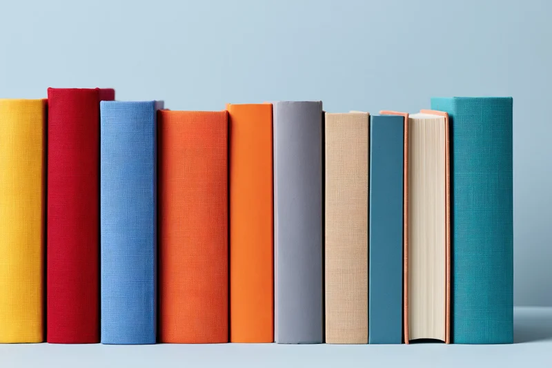 Row of colorful hardcover books standing upright on a flat surface with copyspace on light blue background