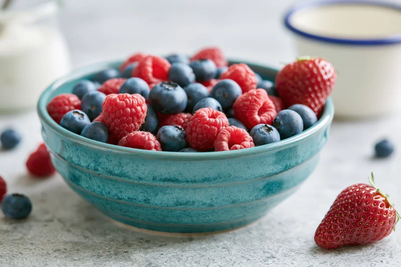 Turquoise ceramic bowl filled with fresh mixed berries on a gray countertop