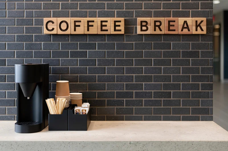 Self-serve coffee station with wooden sign on black brick wall and concrete counter