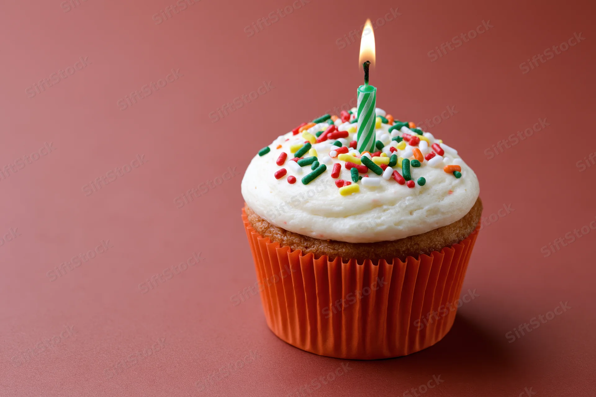 Single birthday cupcake with lit candle and colorful sprinkles on pink surface