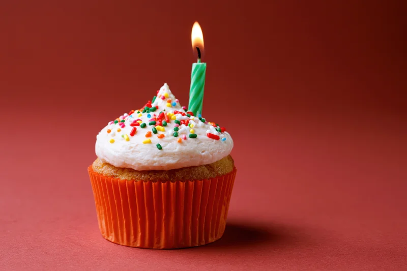Single birthday cupcake with lit candle and sprinkles on red background