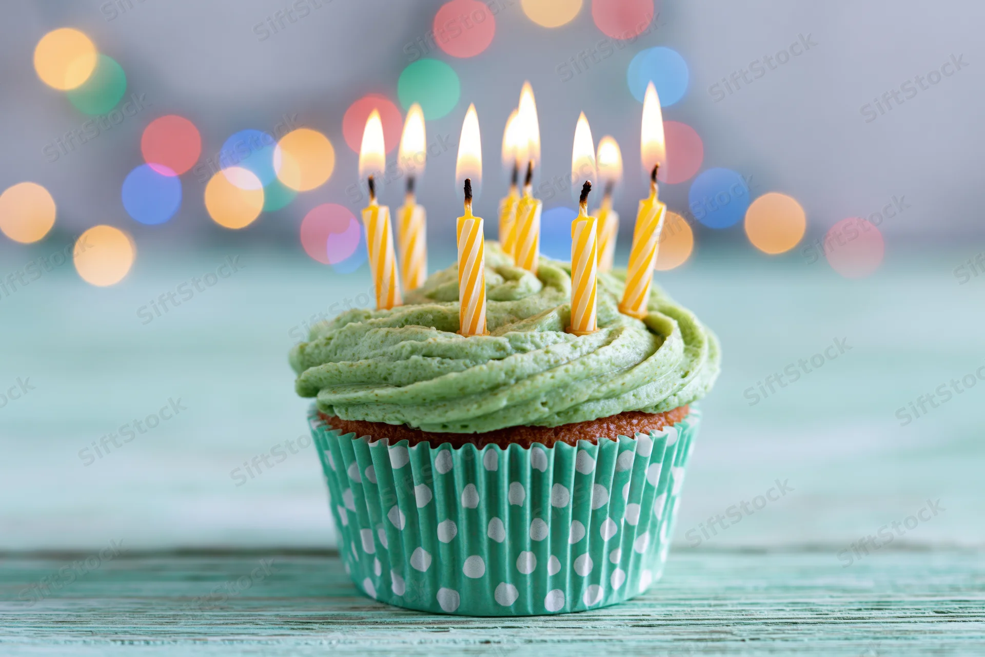Single birthday cupcake with green frosting and lit candles on a teal wooden surface