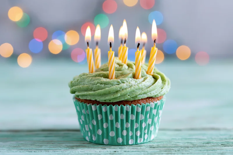 Single birthday cupcake with green frosting and lit candles on a teal wooden surface