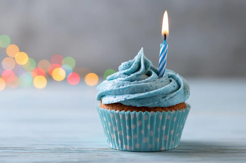 Single birthday cupcake with blue frosting and lit candle on wooden table