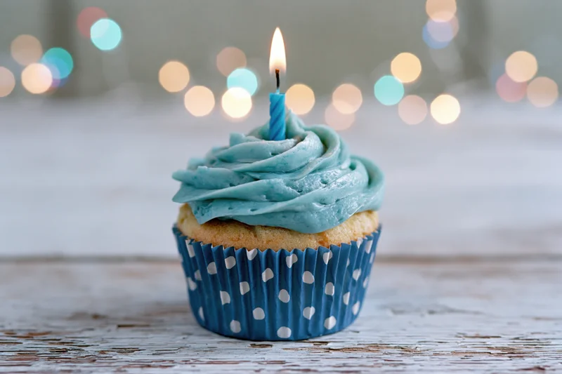 Single birthday cupcake with blue frosting and lit candle on wooden table