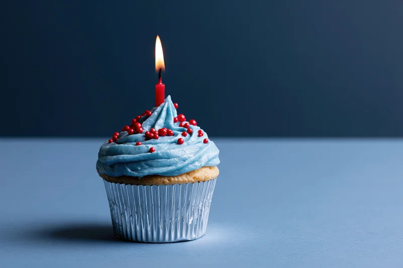Single birthday cupcake with blue frosting and lit red candle on a blue surface