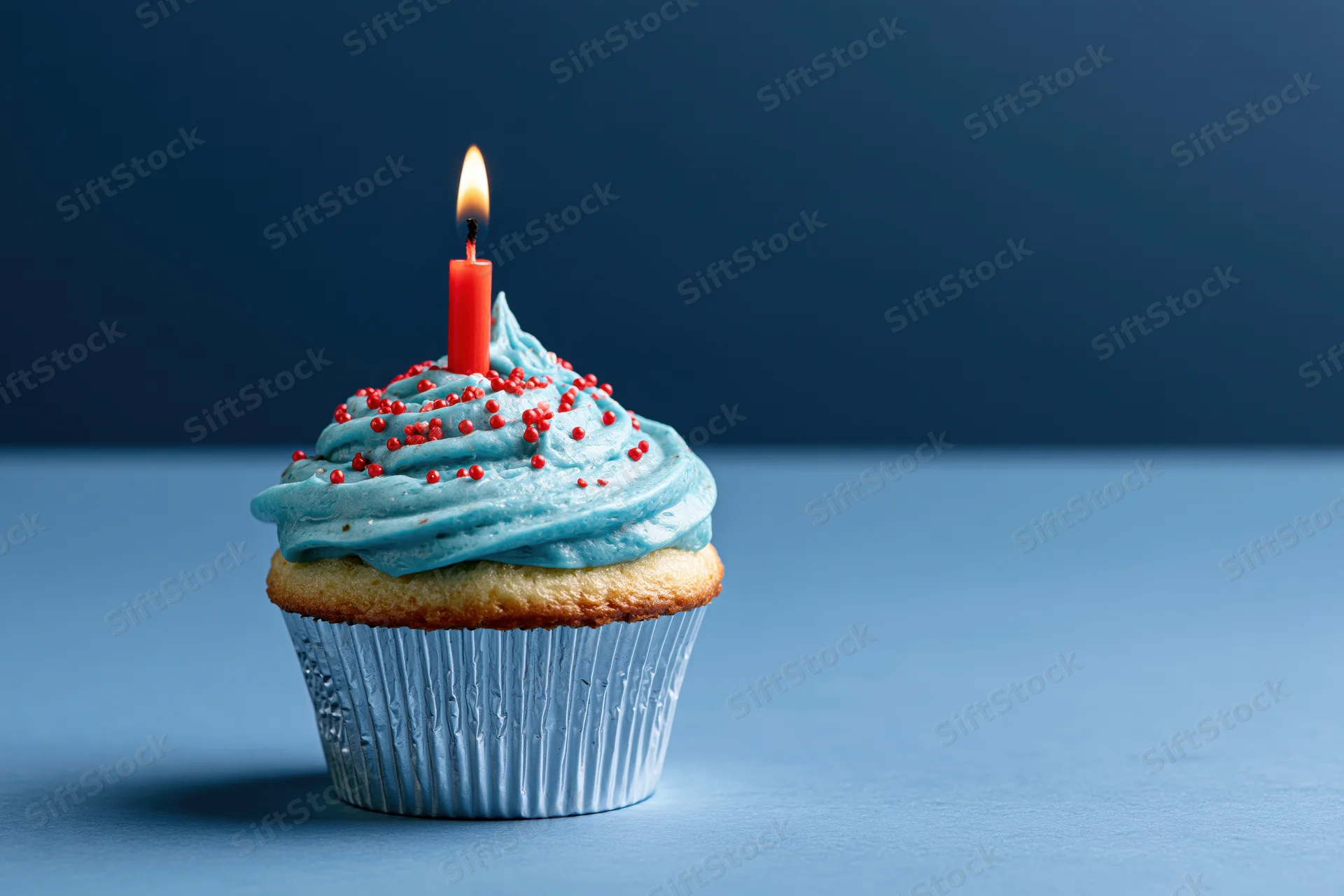 Single birthday cupcake with blue frosting and red candle on blue surface