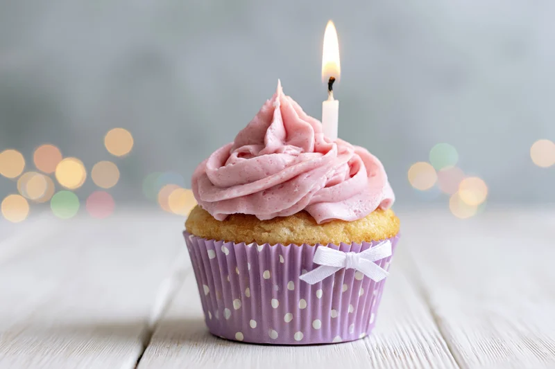 Single birthday cupcake with pink frosting and lit candle on wooden table