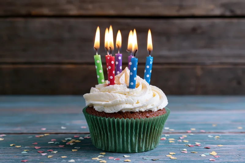 Single birthday cupcake with lit colorful candles and white frosting on wooden table