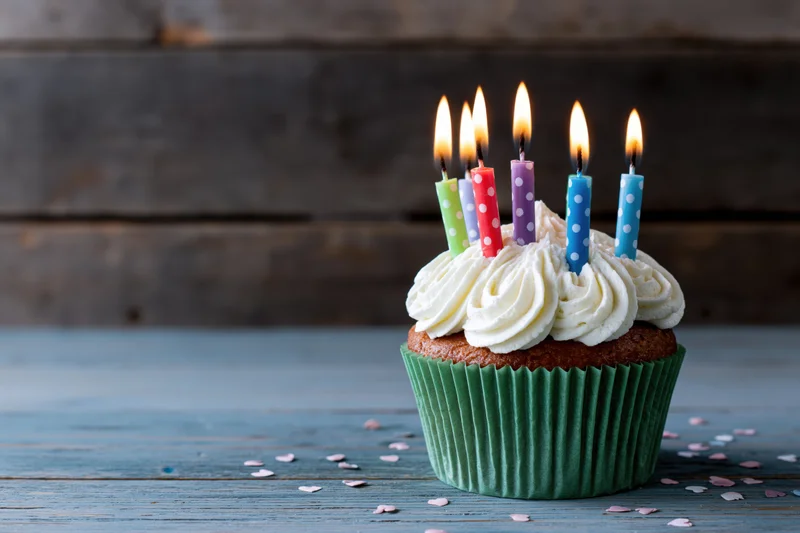Birthday cupcake with lit candles and white frosting on a blue wooden table