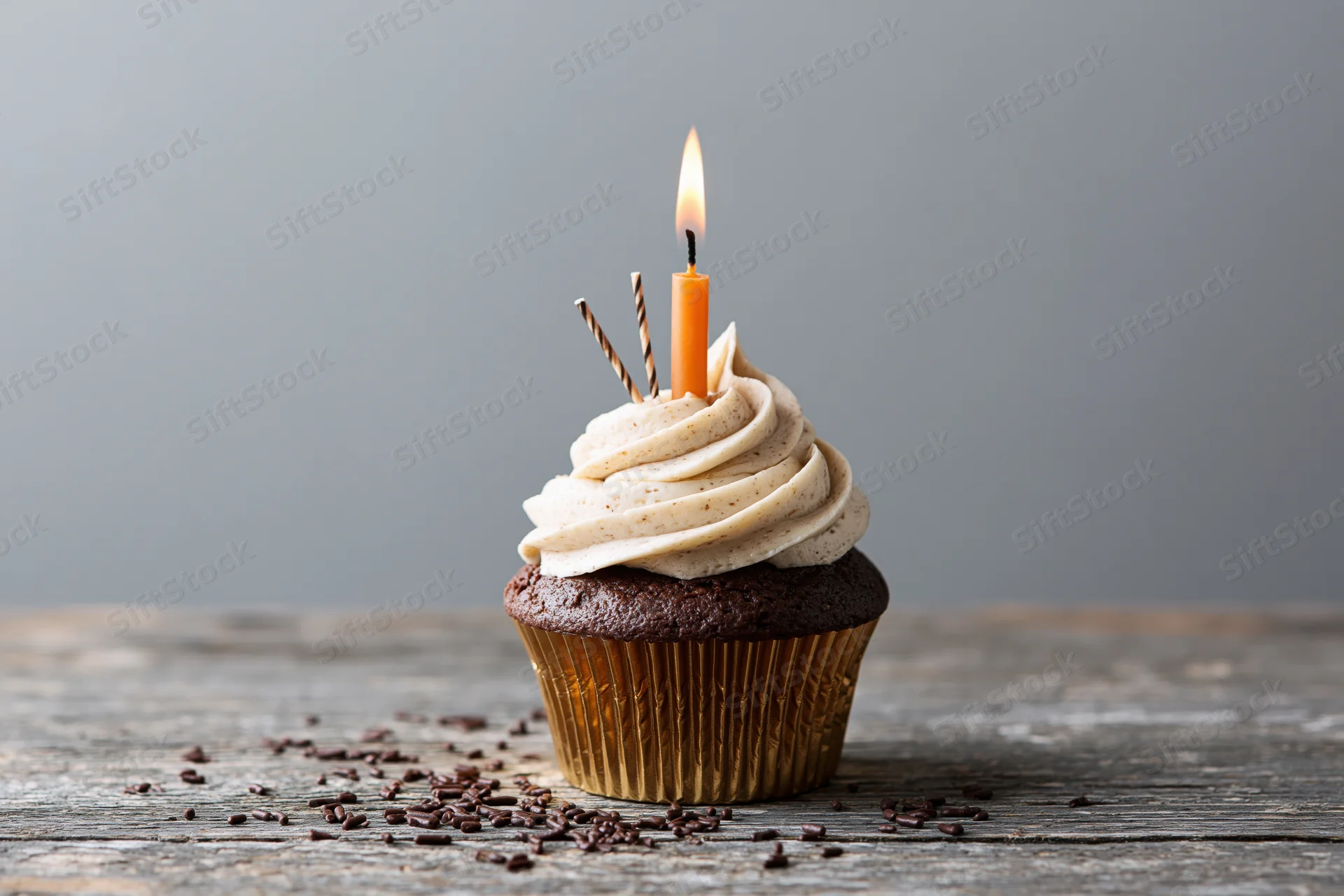 Chocolate cupcake with swirled cream frosting and lit candle on rustic wooden table