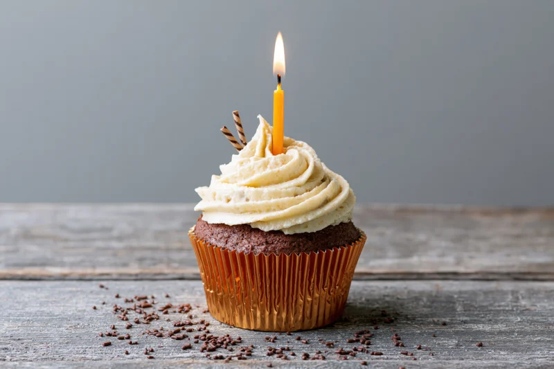 Chocolate cupcake with cream frosting and lit candle on wooden table